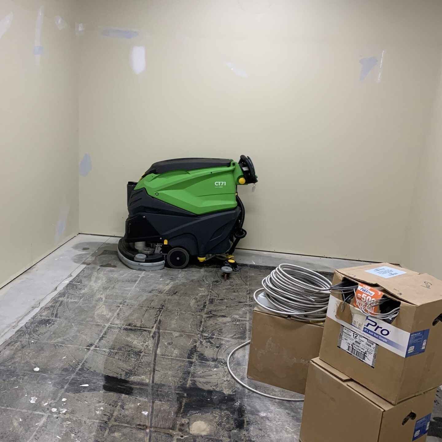 Green floor scrubber next to electrical boxes in a room under renovation.